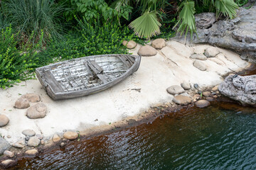 An old, weathered wooden rowboat rests on a small, sandy beach bordered by lush tropical foliage...