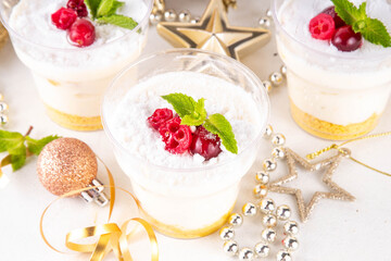 Christmas portioned cheesecakes in glass, made from golden sugar cookie crumble, layered with white mascarpone cream cheese, sugar powder and cranberry decor, copy space
