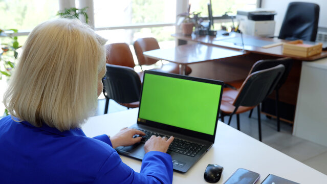Experienced female executive using a laptop with a green screen, chroma key, in a contemporary office, providing options for tailored content and presentations - Powered by Adobe
