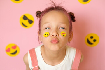 Funny girl with smiley icons pasted on her face and pink studio background. World Social Media Day. Using emoji to convey emotions in messages and social networks.