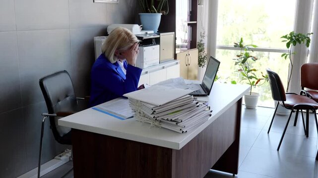 Businesswoman is getting increasingly frustrated while working with documents at her desk. She eventually puts her head in her hands