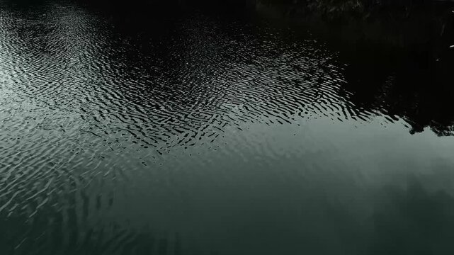 Dark mysterious video of slow breeze on water. Still lake water and small waves. 