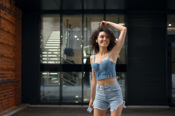 Happy young woman in denim outfit dancing to music with wireless earbuds, holding a smartphone...