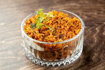 Glass bowl with creamy base and golden breadcrumb topping, garnished with fresh herbs. Rustic presentation on wooden surface. Ideal for gourmet or lifestyle food themes.