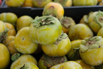 A black crate is filled with ripe Fuyu persimmons
