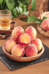 Fresh ripe peaches in wicker basket on rustic wooden table with cut fruit showing juicy flesh