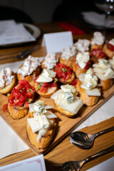 Assorted gourmet bruschetta on wooden platter featuring creamy cheeses and fresh tomato toppings served during elegant dinner event