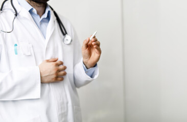 A close-up shot of a doctor wearing a white coat and holding a pen. The doctor has a stethoscope around their neck. Concept for healthcare and m