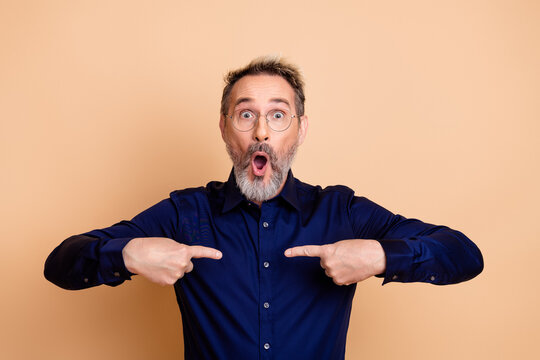 Surprised mature businessman pointing at himself against a beige background - Powered by Adobe