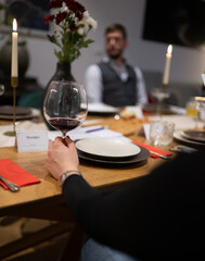 Intimate dinner table with candlelight focusing on wine glass held by hand and blurred person in background during evening meal