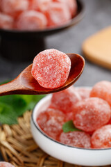 Red sugar-coated kumquat candy on wooden spoon with traditional fruit preserves