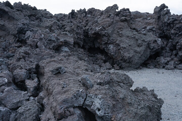 Volcanic rock formations create a rugged landscape with textured surfaces and dark hues, showcasing...