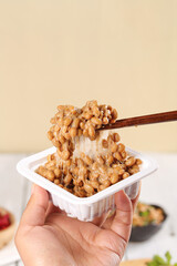 Japanese Natto Fermented Soybeans with Sticky Strings Held by Chopsticks in Small Container