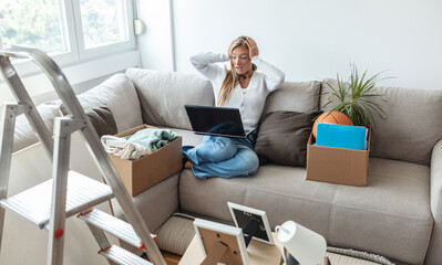 Shocked, stunned young women, dressed in casual wear, sit on sofa between cardboxes with things...