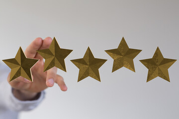 A hand reaching towards a group of five gold stars, symbolizing ratings, reviews, and success....