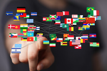 A person's hand pointing towards a network of global flags, representing connection, international...