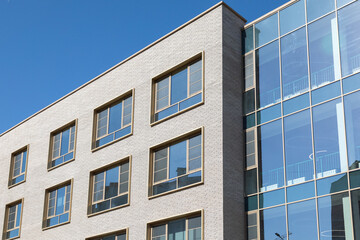 Modern building facade with brick and glass panels under blue sky. Clean architectural lines for commercial or residential projects. Real photo