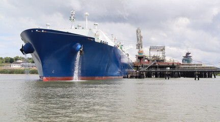 A large tanker ship with a blue hull sits anchored at the oil jetty