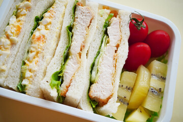 卵サンドとチキンカツサンドを詰めた手作りのお弁当。彩り豊かなミニトマトとキウイが添えられた、家庭的で健康的なランチボックス。