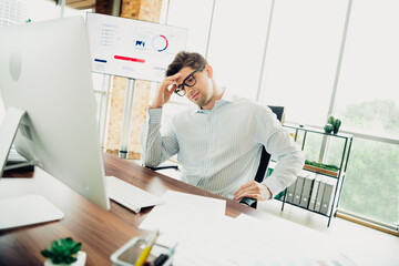Young professional businessman working in office focused on tasks, surrounded by charts and modern workspace environment.