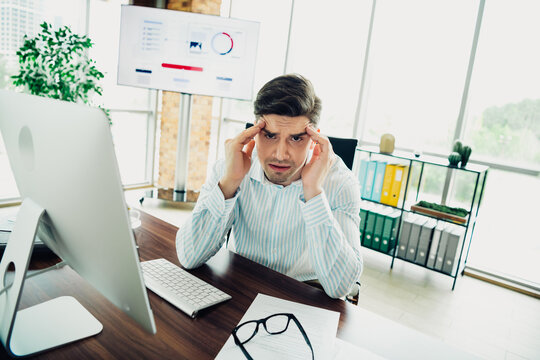 Concerned businessman in an office analyzing reports while sitting at his desk with a computer and documents