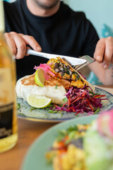 Man cutting a fresh and tasty vegetable burrito filled with black beans served with lime and red salad, enjoying a healthy meal.