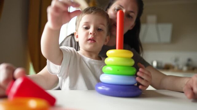 Child stacks colorful ring toy while parent guides toddler hand during play at home mother toddler learns shape recognition and motor skill through playful stacking learning and parent bonding