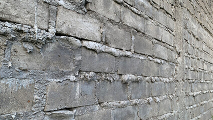 Detailed side-angle view of a weathered exterior wall constructed from rough gray concrete cinder blocks joined by thick, unevenly textured white mortar. Construction concept