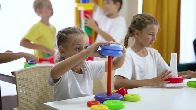 Children play with stacking toy and learning game as girl and boy sort colorful ring on table in classroom while kids concentrate on fine motor practice and cooperative play with plastic stacker