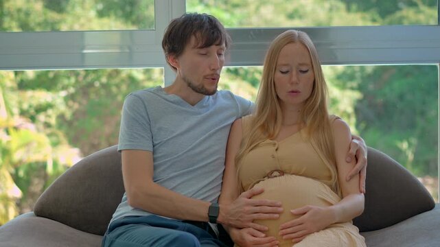 Caring husband supports his pregnant wife as they practice breathing exercises together to ease tension during early labor contractions and prepare for childbirth. Slowmotion video.