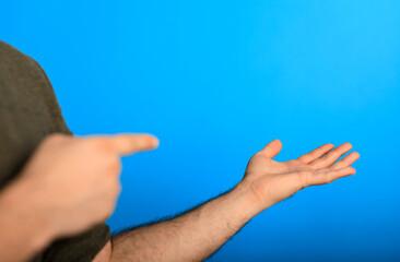 Man with outstretched arm and pointing finger showing or presenting something against a blue background, representing concepts like offering or