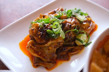 A plate of Chinese-style dumplings served with a rich, spicy chili oil sauce and topped with freshly chopped scallions