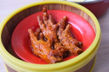 A serving of braised chicken feet, a popular dish in Chinese dim sum, presented in a red dish...