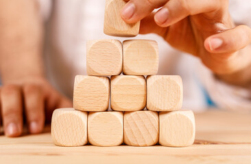 A hand carefully places the final wooden block to complete a structure representing business concepts and success. Building, teamwork, and growt