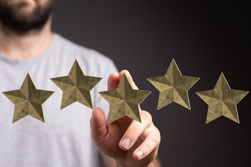 A close-up shot of a man's hand touching five gold stars, symbolizing ratings, success,...
