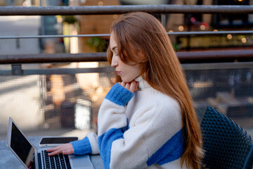 Young woman working on a laptop at a cozy urban cafe in the afternoon