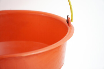 A close-up, angled shot of an empty, bright orange plastic bucket with a small section of its...