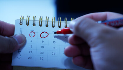 A person marks a calendar with a red marker, circling dates and marking deadlines and progress. Time management, planning, scheduling Important days, Deadlines
