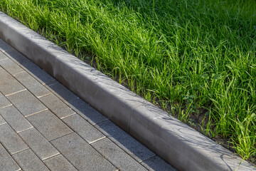 Obraz premium Paving with curb and green lawn on landscaped grounds. Diagonal arrangement