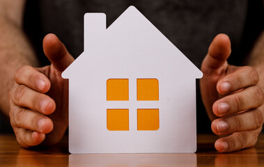 Hands cradling a paper house, symbolizing home security, real estate, and property protection....