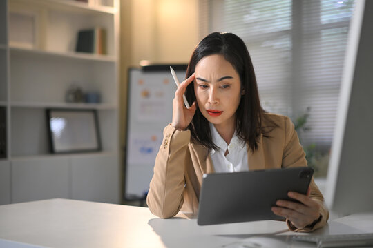 Stressed businesswoman looking at digital tablet in office, facing challenges with work, finance, or business decisions