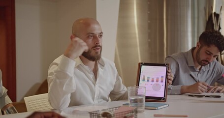 A diverse team of business professionals collaborates on a project, analyzing charts and graphs on a tablet and paperwork in a modern office. - Powered by Adobe