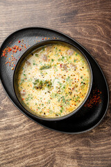 Creamy soup served in a bowl on a black plate, garnished with herbs and spices. Rustic wooden background adds warmth and contrast. Top view, close-up, food styling.