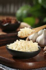 Fresh Minced Garlic from Shandong Farm in Wooden Spoon and Bowl on Rustic Kitchen Table