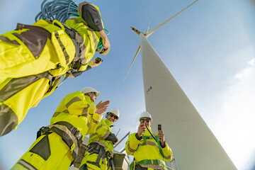 A team of engineers celebrates success after completing wind turbine maintenance at a wind farm....