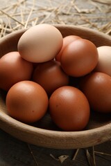 Raw chicken eggs in bowl and straw on wooden table, closeup