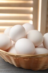 Raw chicken eggs in wicker basket on grey wooden table indoors, closeup