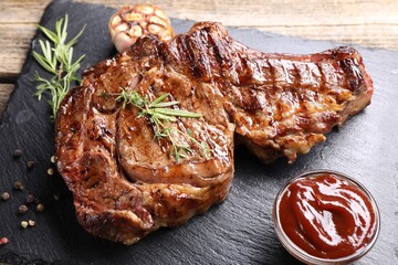 Delicious grilled beef steak with herbs, spices and ketchup on wooden table, closeup