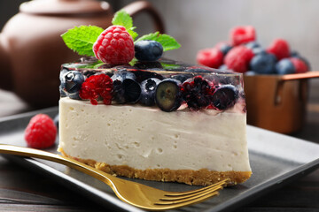Piece of delicious cheesecake with berries, mint and fork on wooden table, closeup