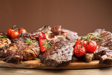 Pieces of tasty grilled beef with rosemary and vegetables on wooden table, closeup